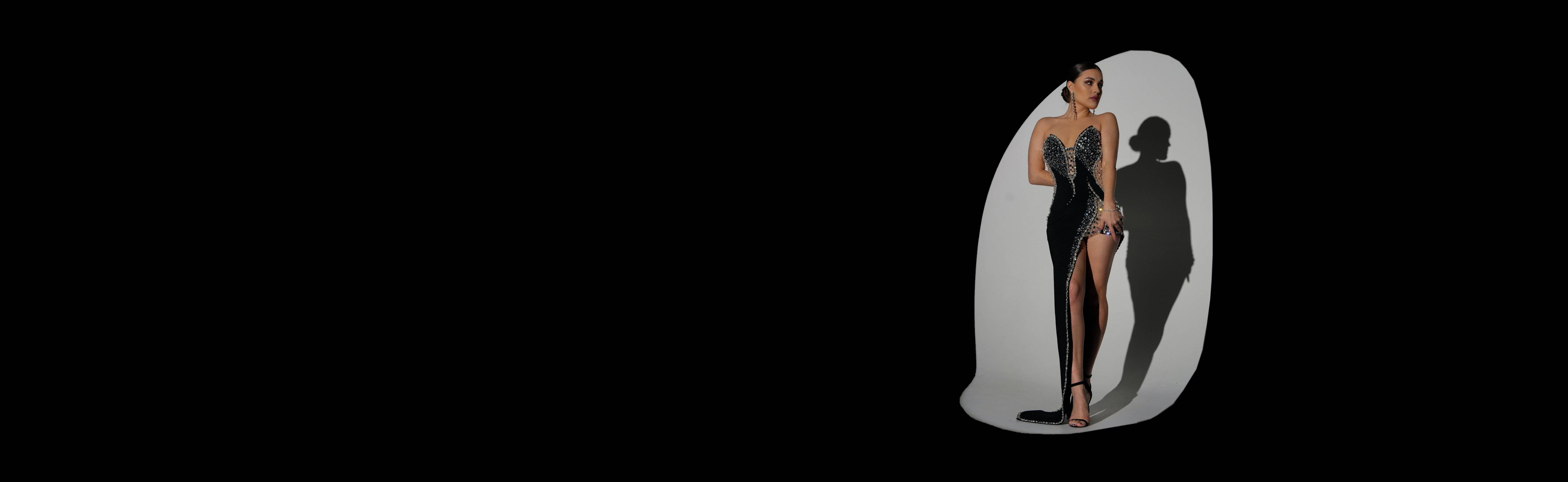 Model wearing a stunning black couture gown with full rhinestone embellishment and a high slit, spotlighted against a black background.