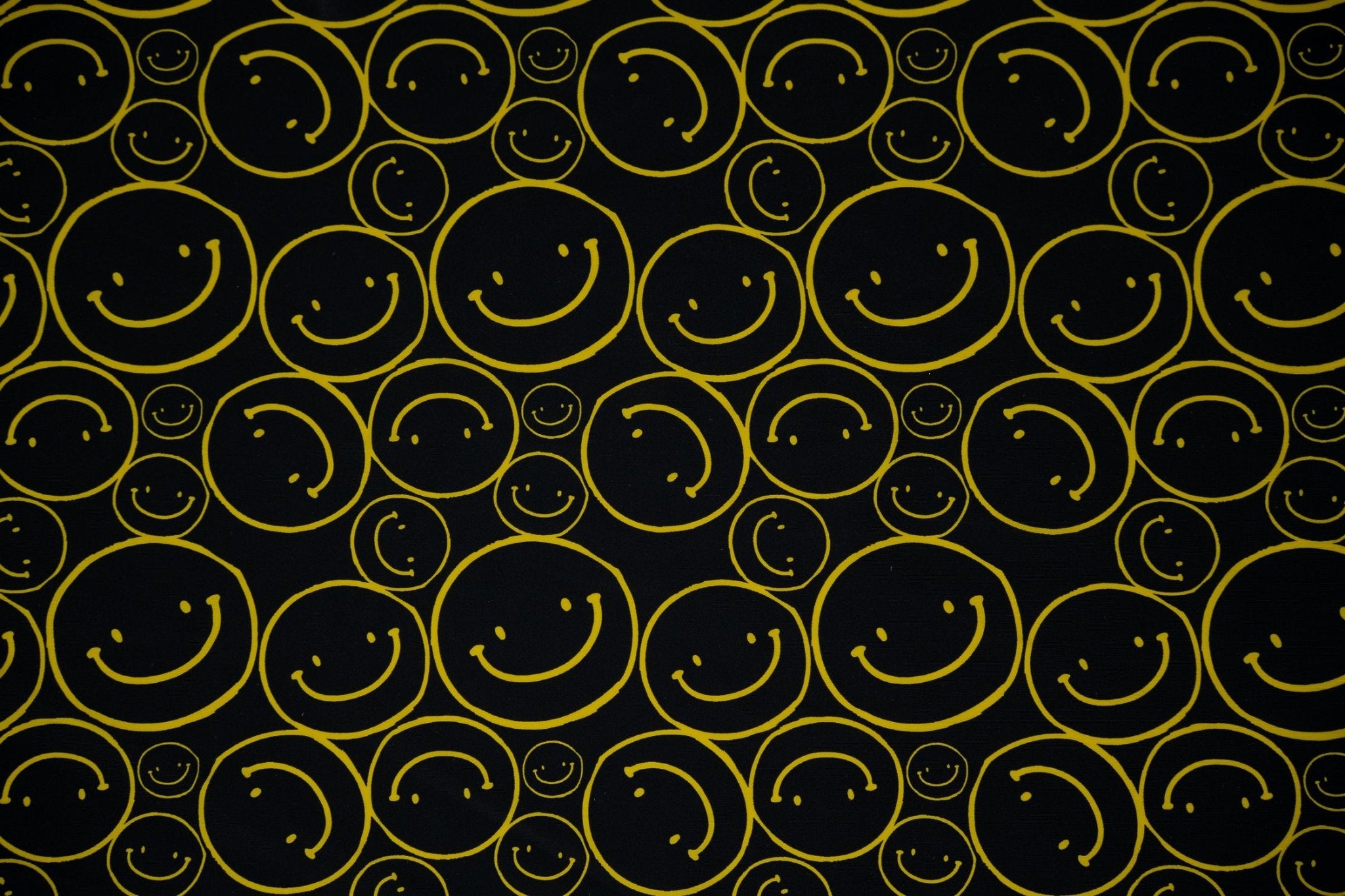 Flat sample shot of All Smiles Printed Spandex. The print is of vibrant yellow smiley faces of various sizes on a black background.