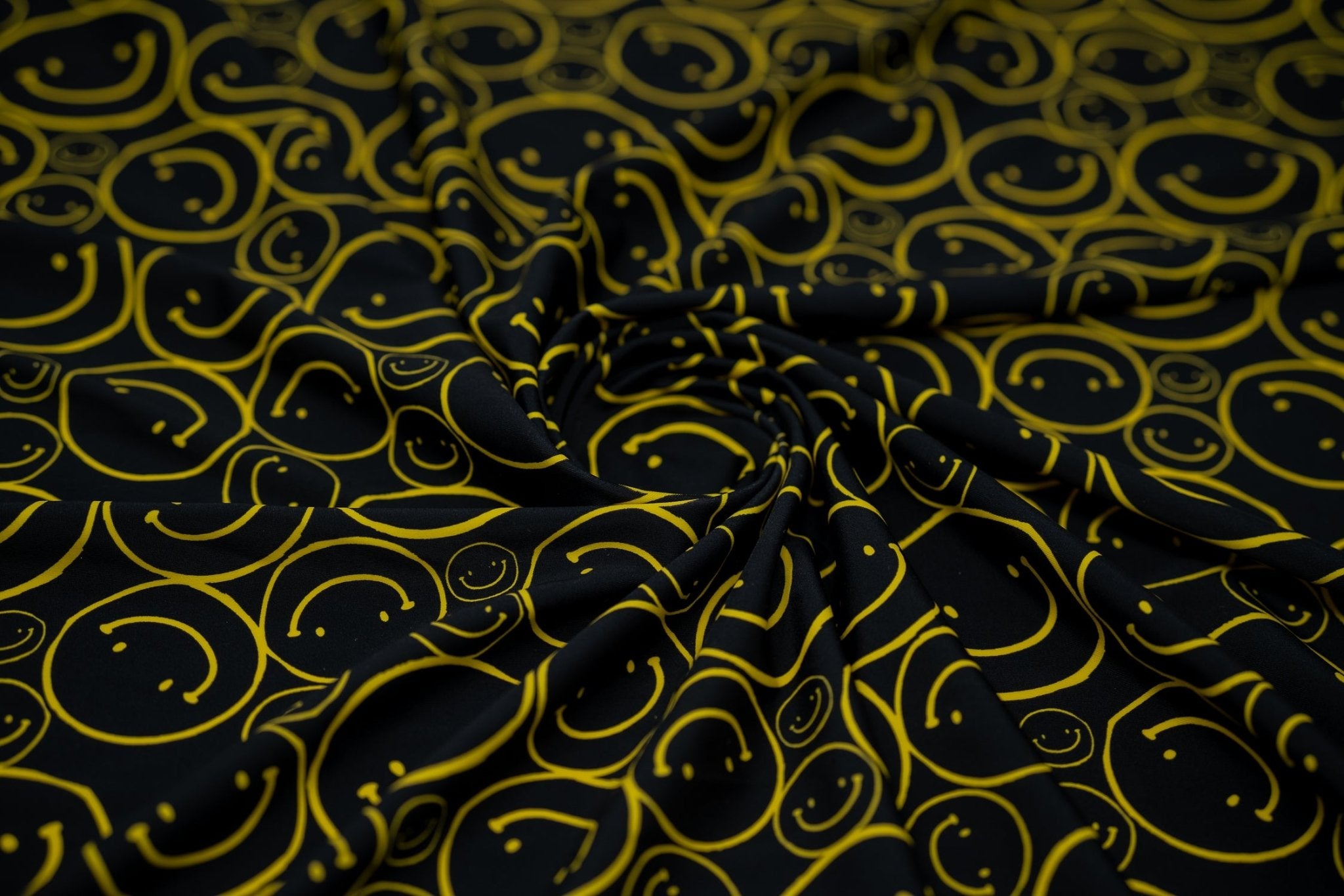 Swirled sample shot of All Smiles Printed Spandex. The print is of vibrant yellow smiley faces of various sizes on a black background.