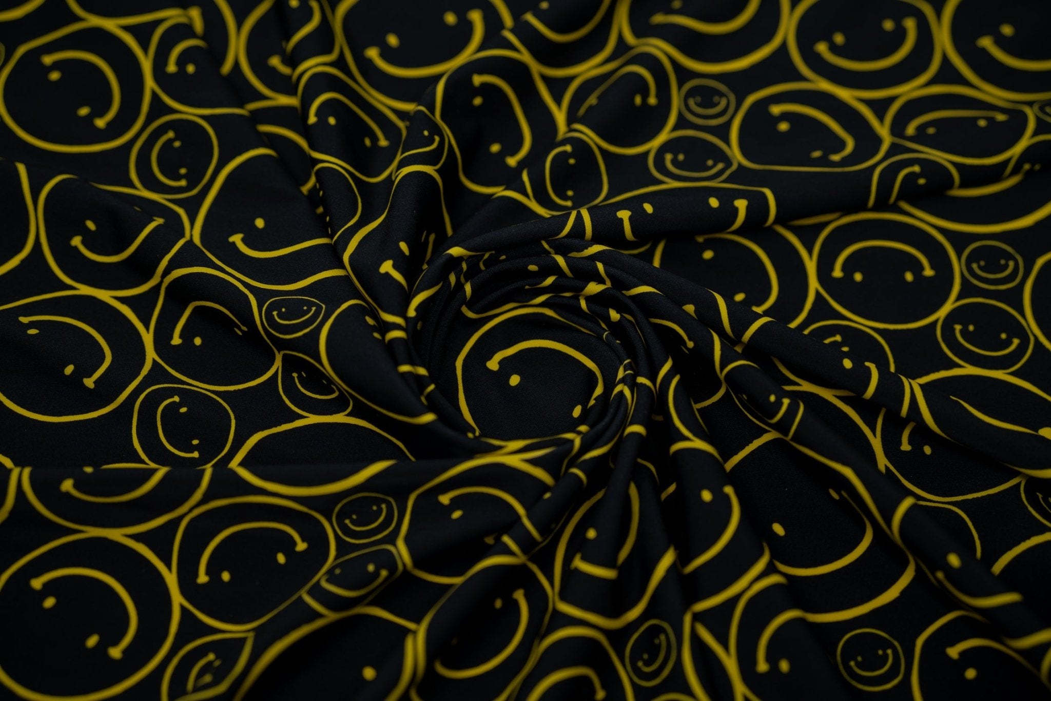Swirled sample shot of All Smiles Printed Spandex. The print is of vibrant yellow smiley faces of various sizes on a black background.