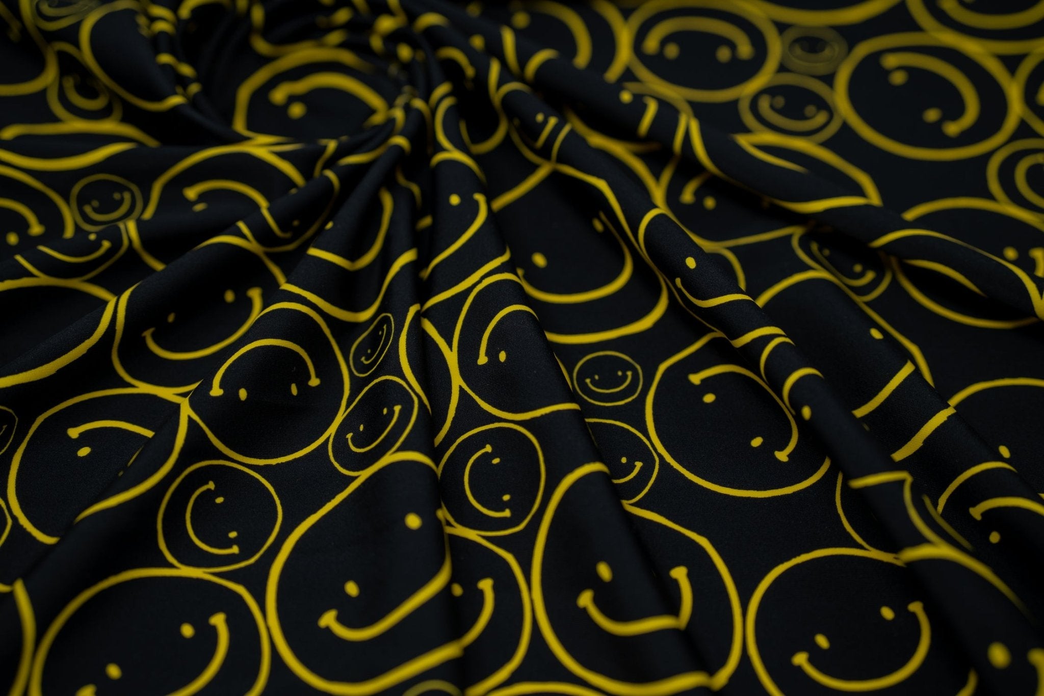 Swirled sample shot of All Smiles Printed Spandex. The print is of vibrant yellow smiley faces of various sizes on a black background.