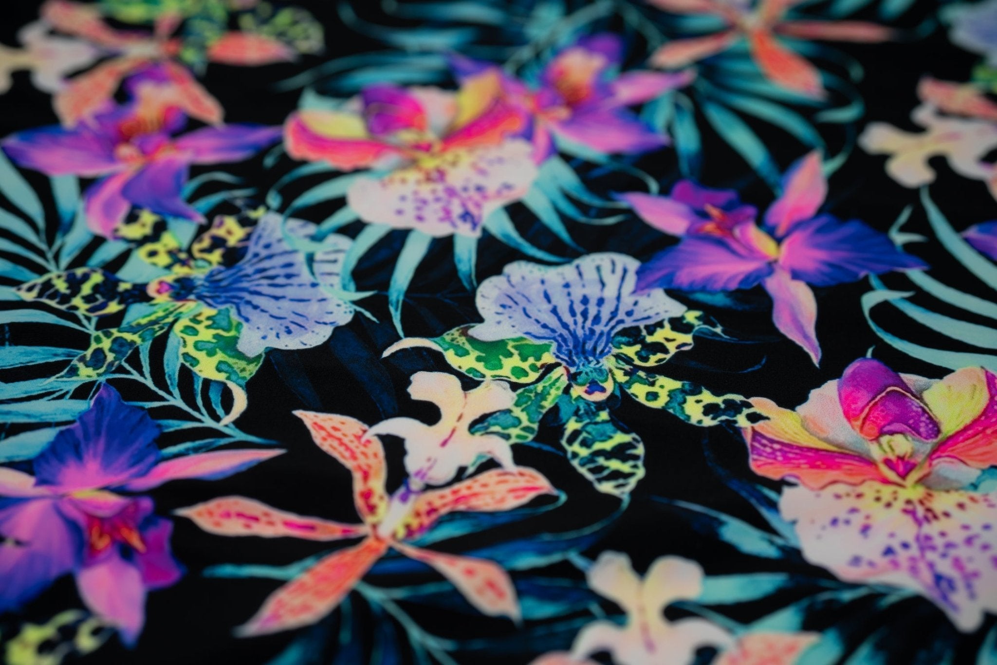 Flat sample of Irises and Palm Fronds Printed Spandex Fabric. The print is of vibrant colored Irises and other exotic flowers over bright light blue fronds on a black background.