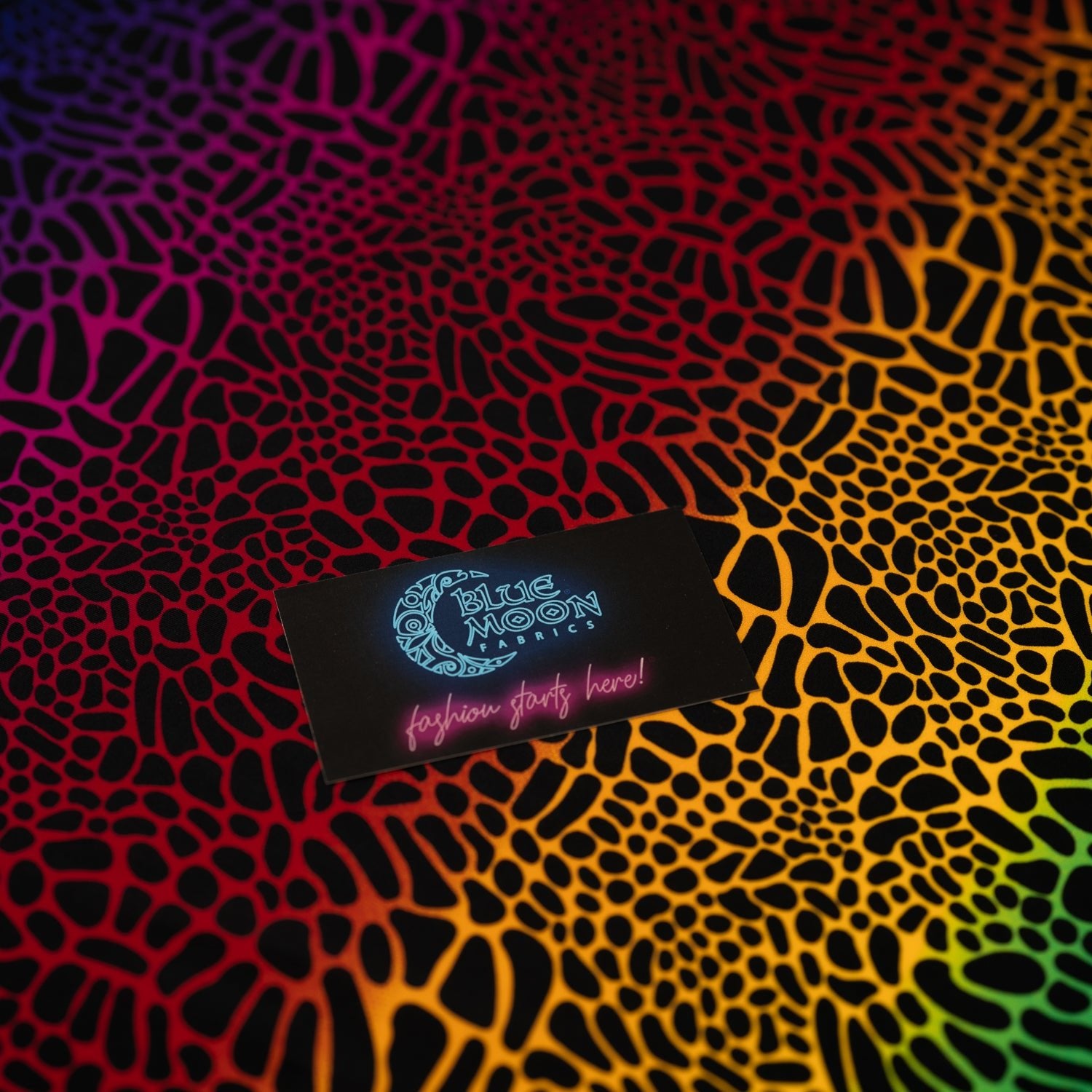 A flat sample of Multicolor Safari Spots Printed Spandex with a Blue Moon Fabrics standard size business card laid on top of the print for pattern sizing.