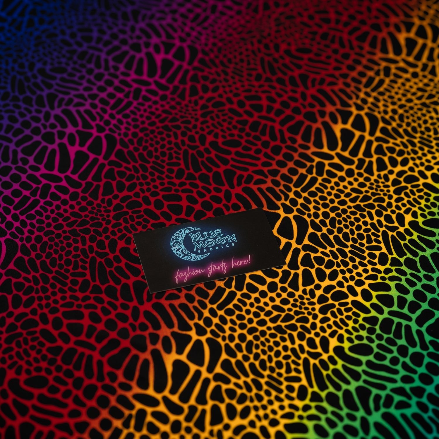 A flat sample of Multicolor Safari Spots Printed Spandex with a Blue Moon Fabrics standard size business card laid on top of the print for pattern sizing.