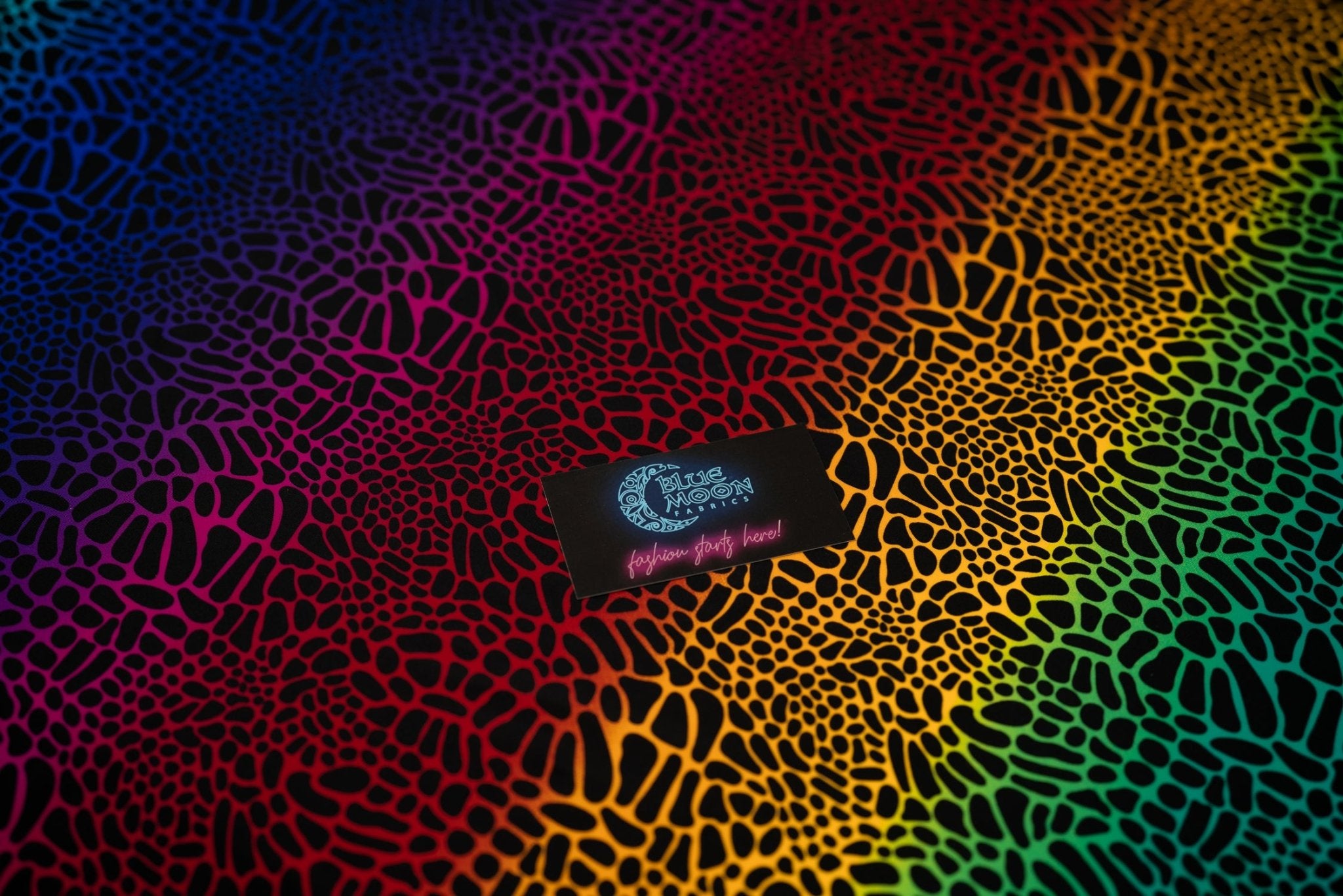 A flat sample of Multicolor Safari Spots Printed Spandex with a Blue Moon Fabrics standard size business card laid on top of the print for pattern sizing.
