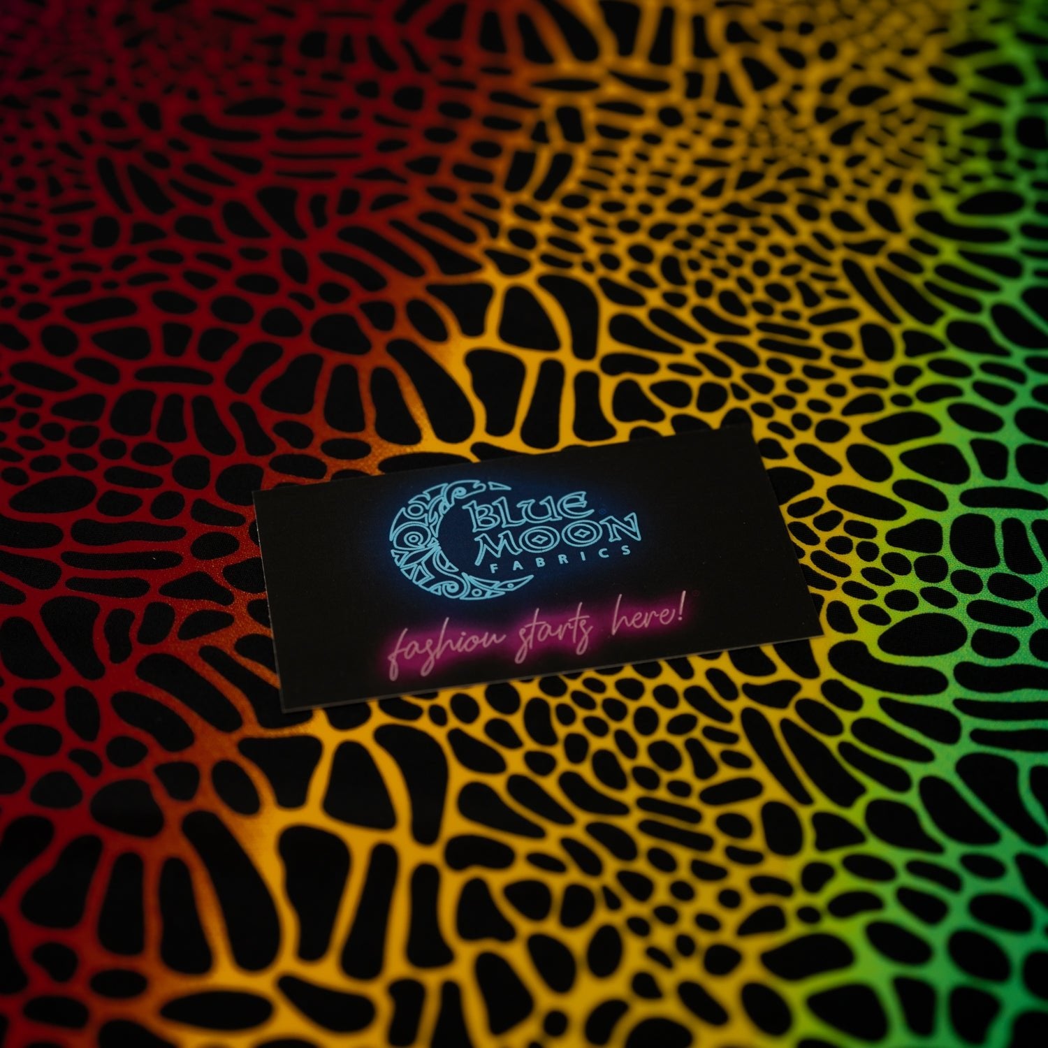 A flat sample of Multicolor Safari Spots Printed Spandex with a Blue Moon Fabrics standard size business card laid on top of the print for pattern sizing.