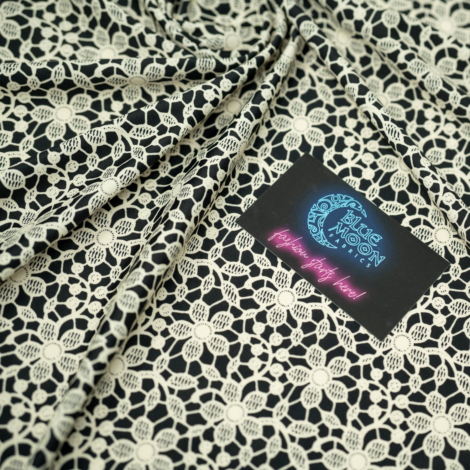 Swirled sample shot of vory Flower Lace Pattern on Black Printed Spandex with a Blue Moon Fabrics standard size business card laid on top of the print for pattern sizing.