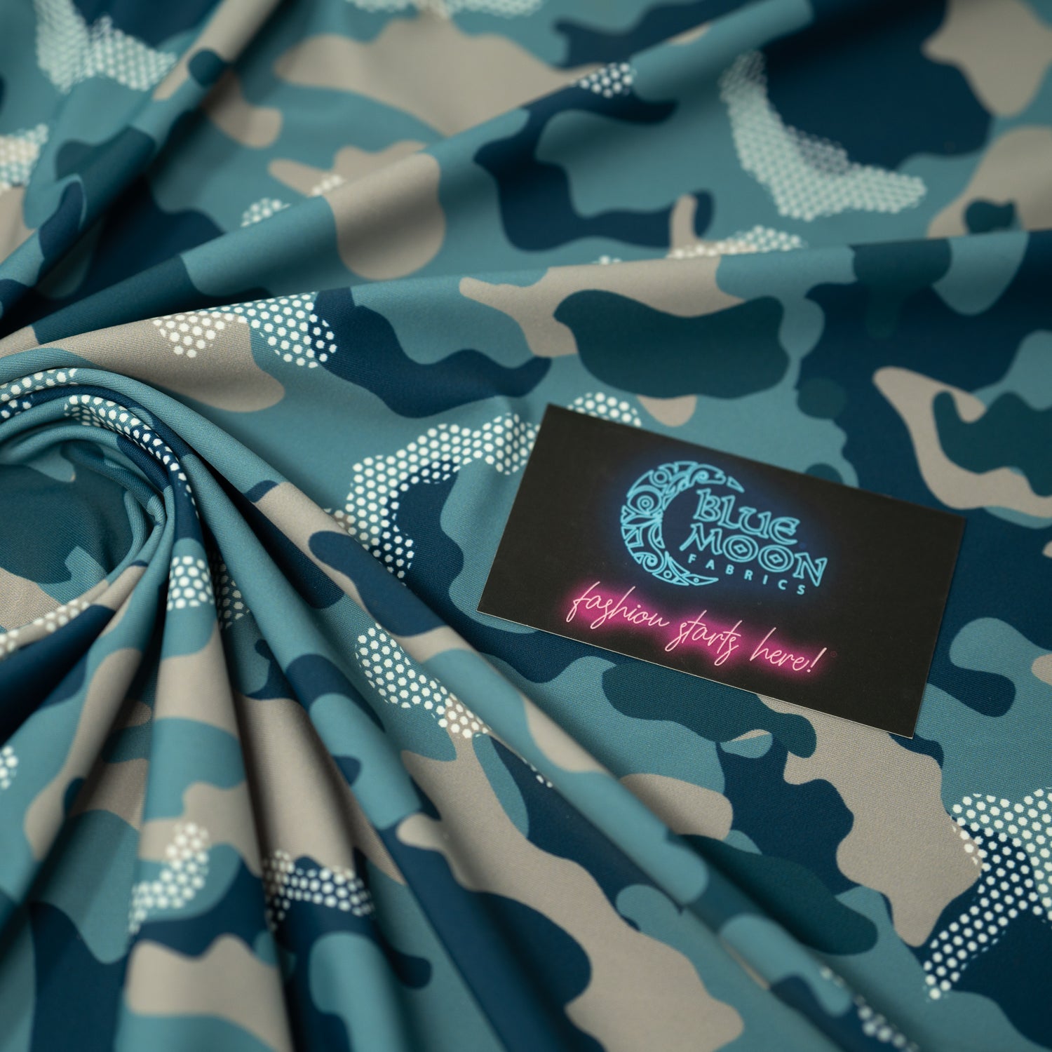 Swirled sample shot of Fiji Camouflage Printed Spandex in the color navy-blue-white-brown with a Blue Moon Fabrics standard size business card laid on top of the print for pattern sizing.