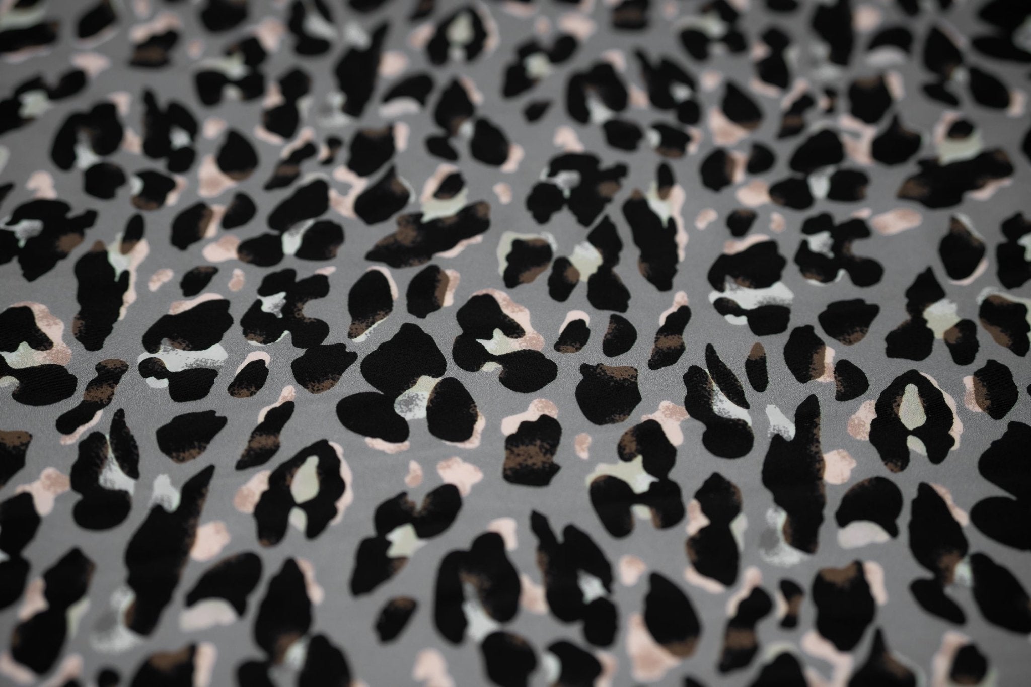 Flat sample shot of Sporty Leopard Printed Spandex Fabric. The print is of black leopard spots with light dust brown accents and light colored shadows on a gray background.