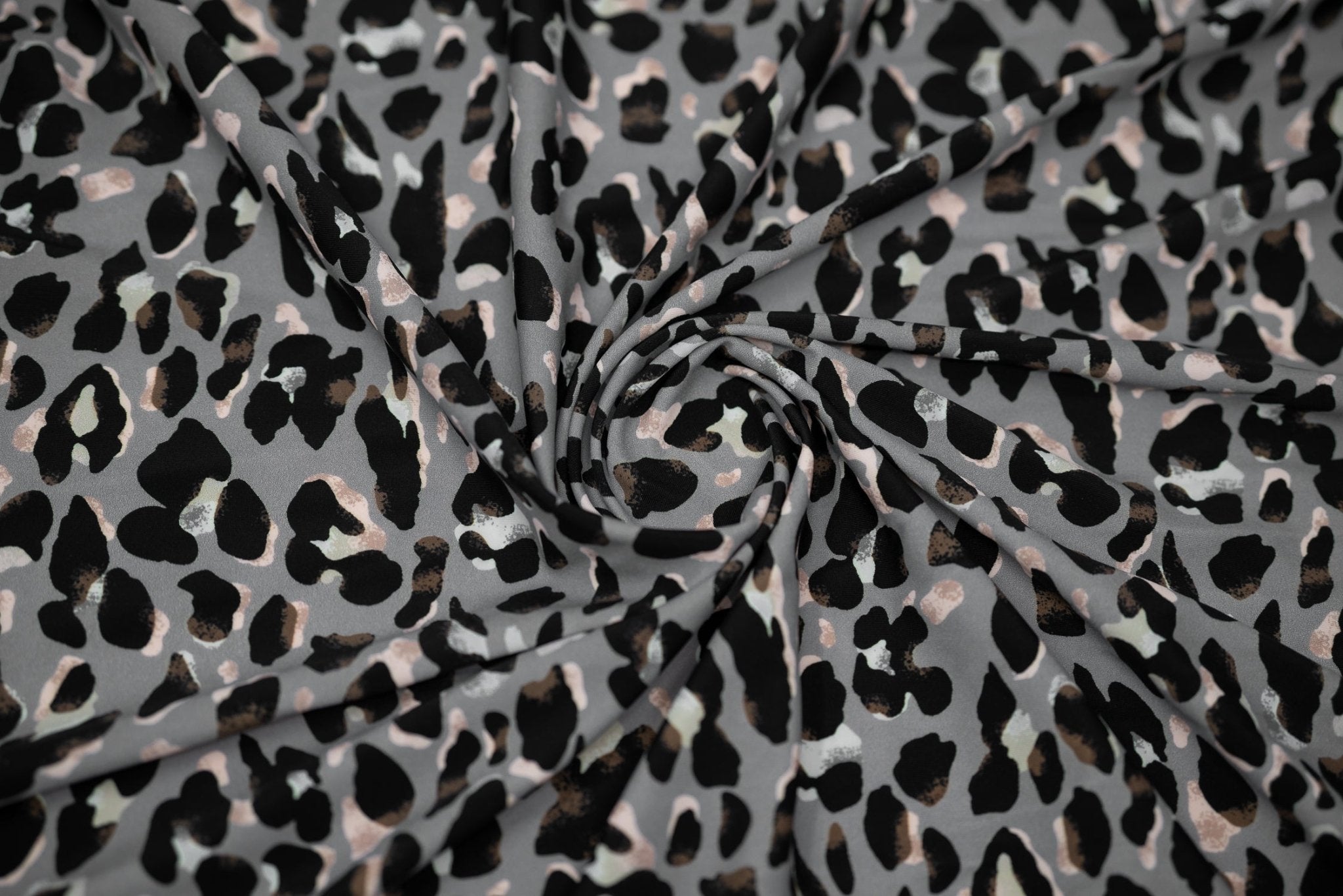 Swirled sample shot of Sporty Leopard Printed Spandex Fabric. The print is of black leopard spots with light dust brown accents and light colored shadows on a gray background.