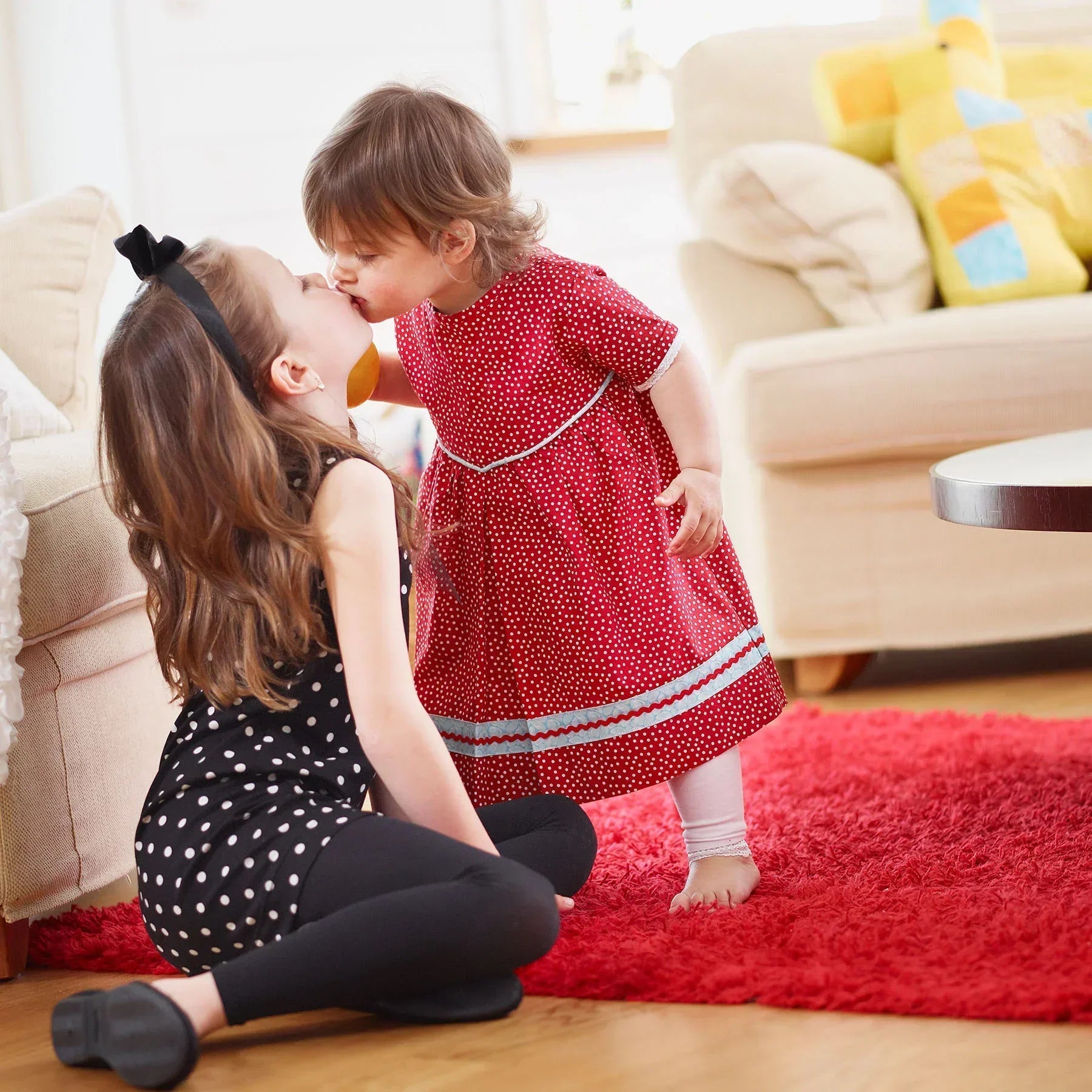 Two young girls playing on a red rug in a living room.