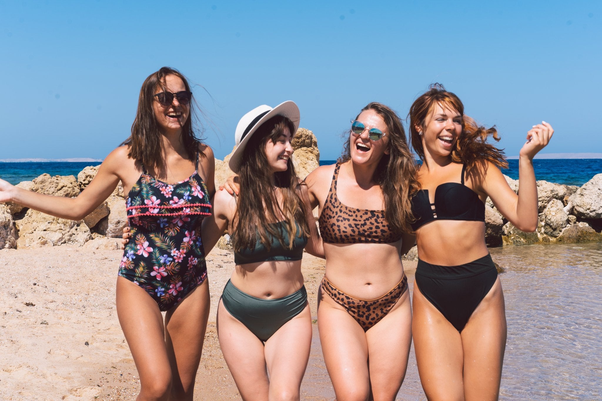 Four women posing in swimwear on a sunny beach.