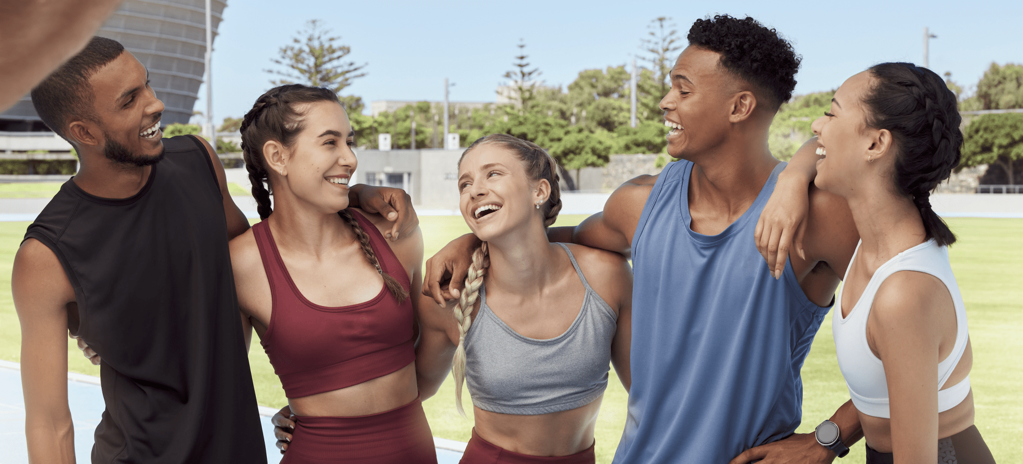 Five young athletes in diverse performance wear at an outdoor track stadium.