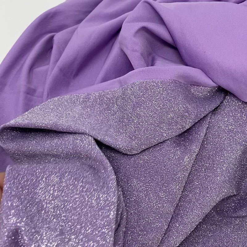 Hands playing with a sample of Deluxe Nylon Spandex 4-way Stretch Lurex fabric stretching pulling and tugging at the piece of material with a bright lilac nylon spandex base and silver metallic fibers on the face.