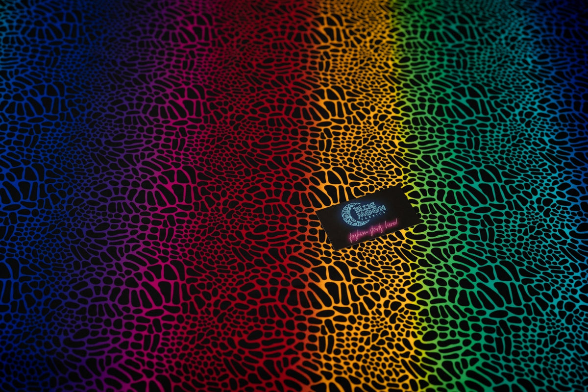 A flat sample of Multicolor Safari Spots Printed Spandex with a Blue Moon Fabrics standard size business card laid on top of the print for pattern sizing.