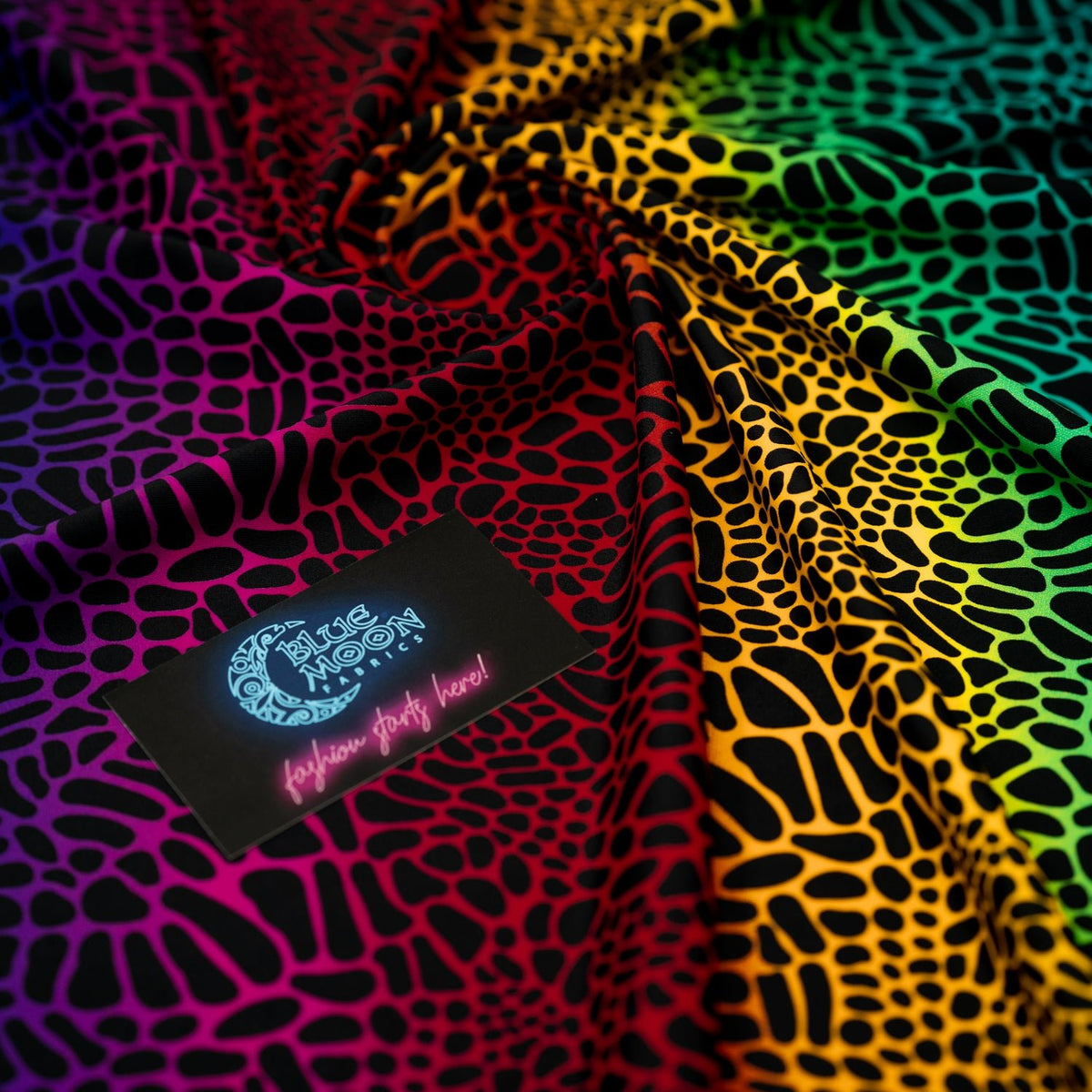 Swirled sample shot of Multicolor Safari Spots Printed Spandex with a Blue Moon Fabrics standard size business card laid on top of the print for pattern sizing.