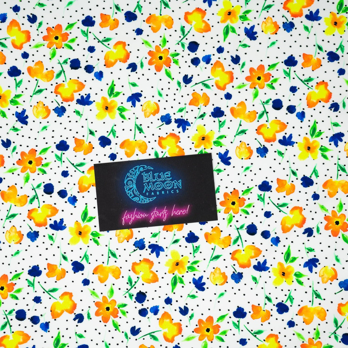 A flat sample of Watercolor Flowers and Black Dots Printed Spandex with a Blue Moon Fabrics standard size business card laid on top of the print for pattern sizing.