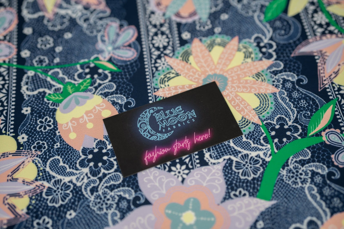 A flat sample of Chantilly Floral Lace Printed Spandex with a Blue Moon Fabrics standard size business card laid on top of the print for pattern sizing.